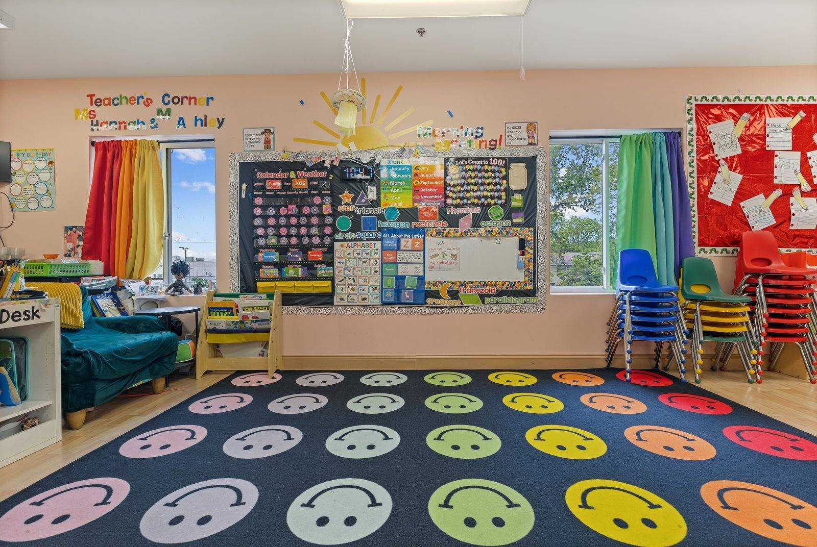 Sunny Days Pre-K classroom in Cherry Hill, NJ: a rug of colorful smiley-face spots faces a calendar and weather board and morning meeting display, with stacked child-size chairs by bright windows.