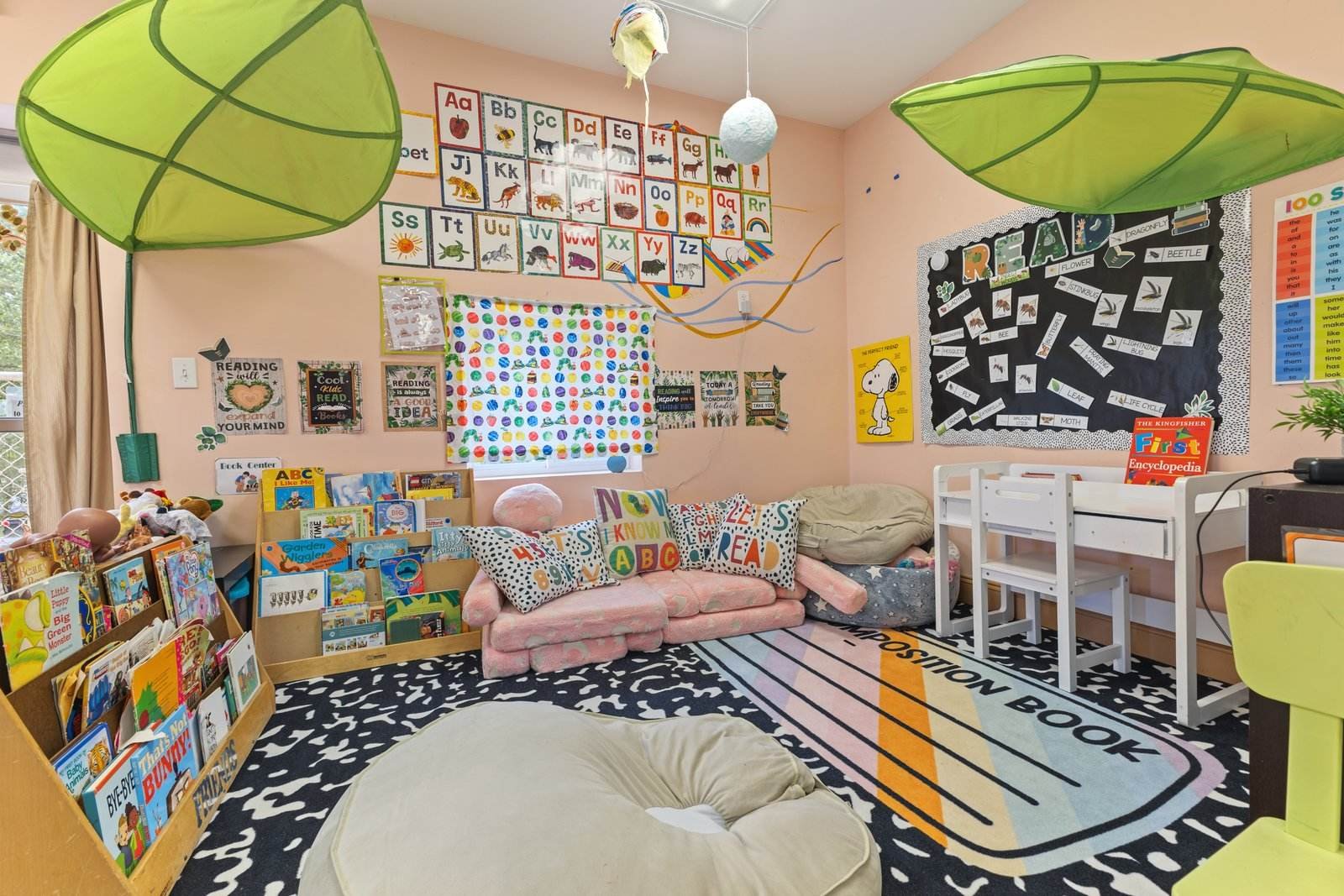 Cozy Pre-K reading corner with a pink foam couch, READ pillows, low shelves of picture books, alphabet cards on the wall and green leaf canopies overhead.